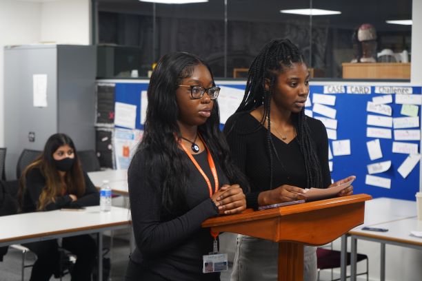 Two black female students speaking from lectern
