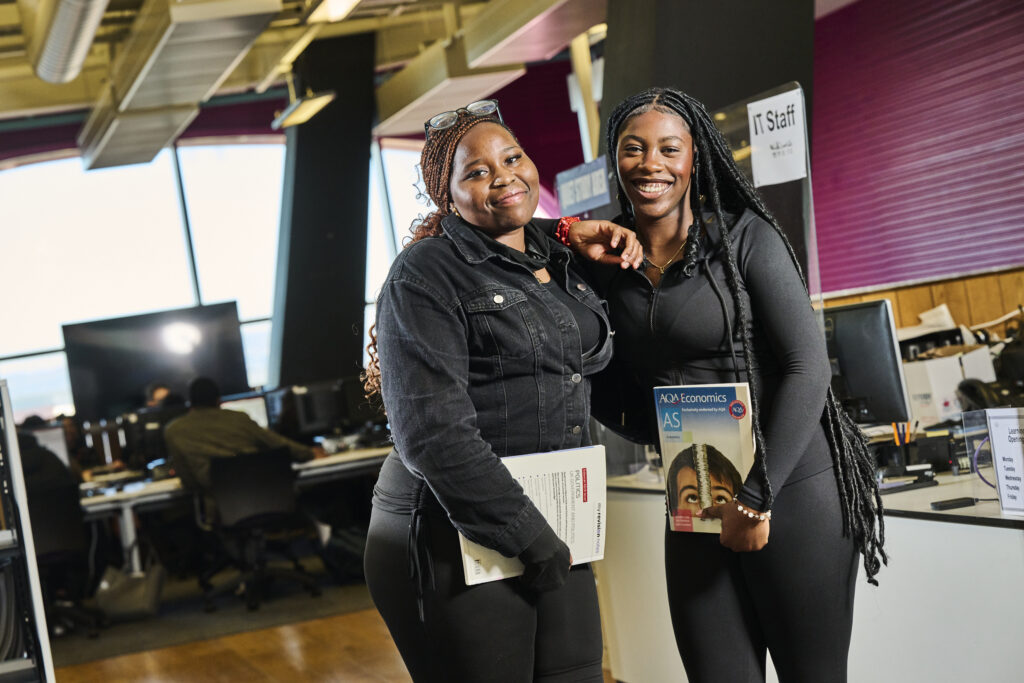 Two female students holding books in the library