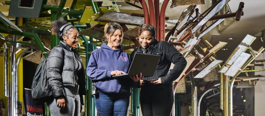 Support Officer showing two female students information on laptop