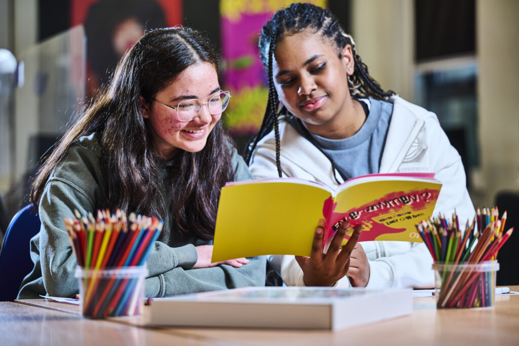 Two students in classroom reading book together