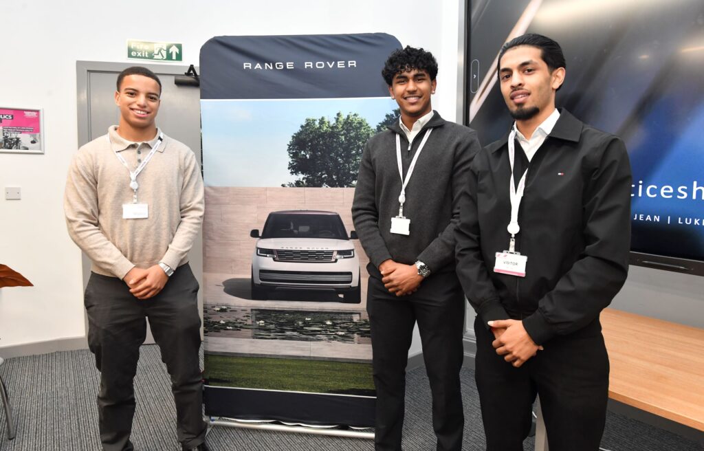 Three engineering degree apprentices from JLR standing in front of a Range Rover banner
