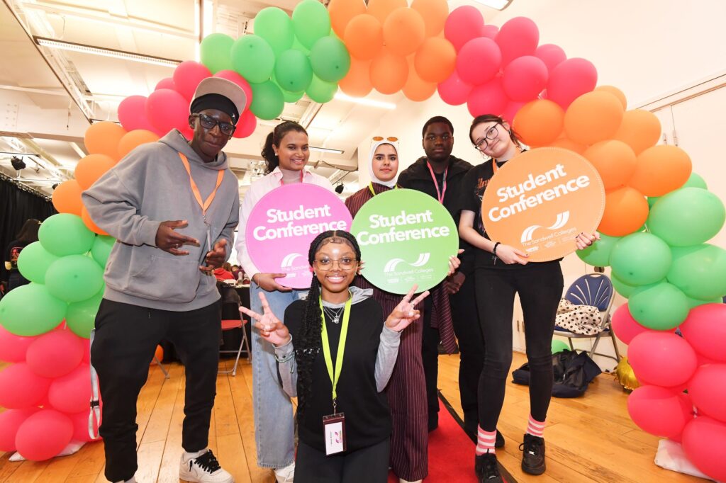 Students holding Student Conference signs under coloured balloon arch
